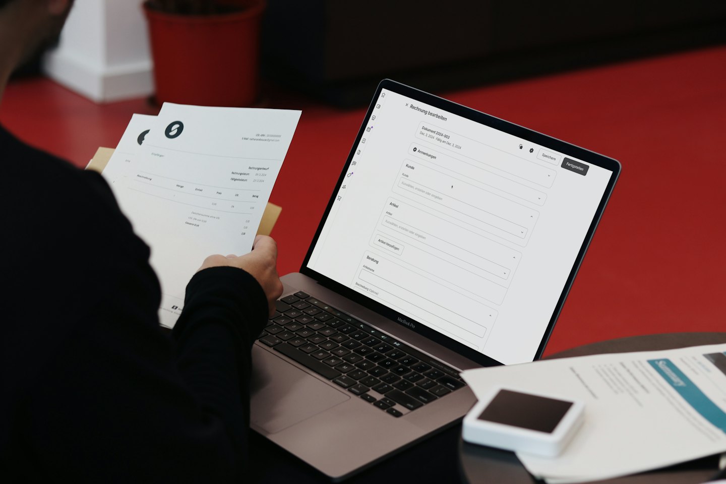 Person edits invoice on laptop with paper document in hand.