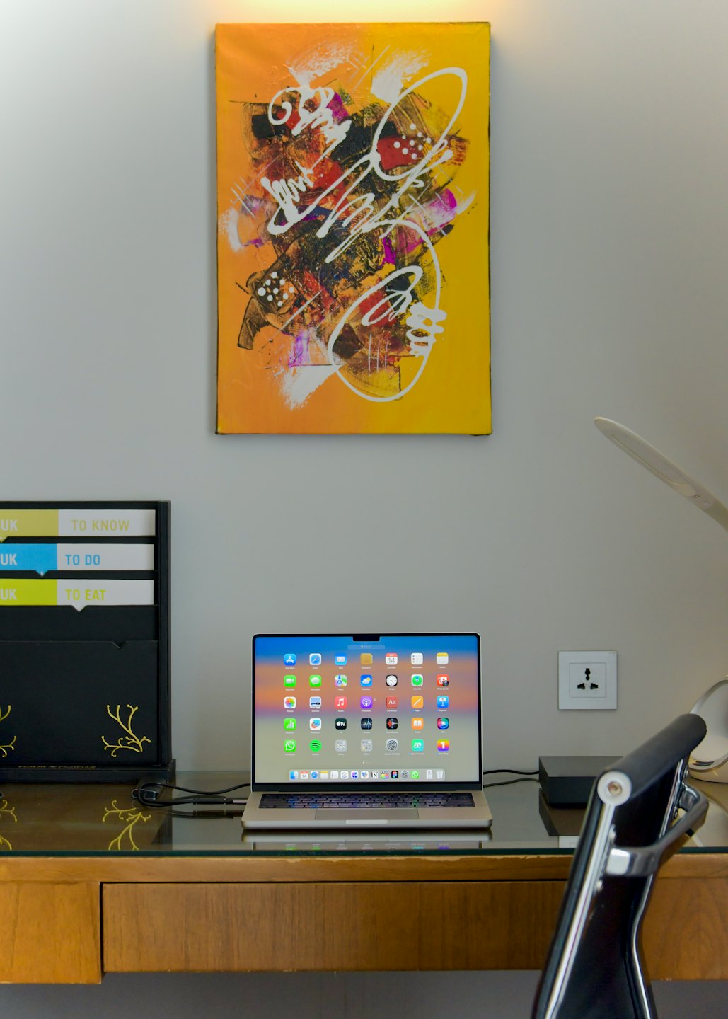 An open silver laptop sits on a wooden glass desk.